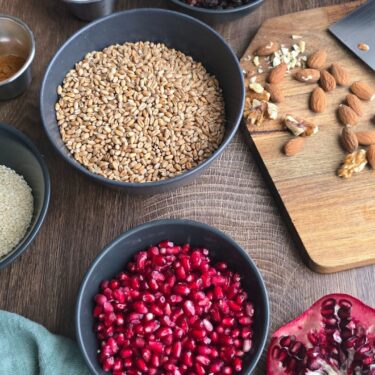 Zutaten für Asure Rezept: Weizen, Granatapfelkerne, Rosinen, Nüsse, Sesam und Honig im Flatlay