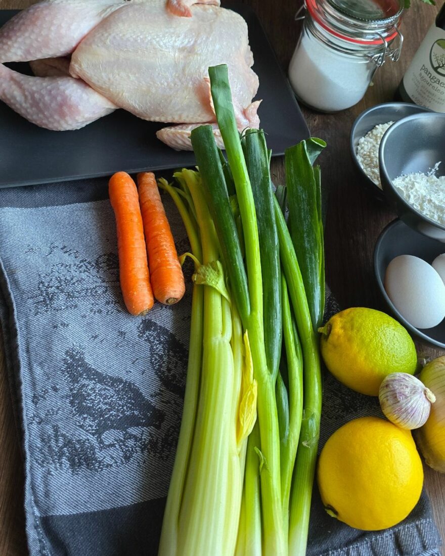 Frische Zutaten für die Avgolemono-Suppe: Huhn, Zitronen, Lauchzwiebeln, Sellerie, Karotten, Eier, Reis und Olivenöl.