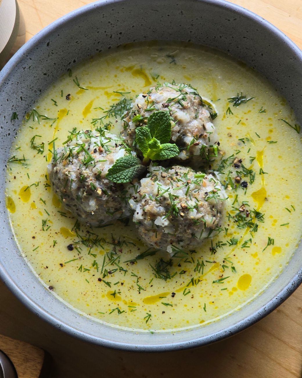 Griechische Giouvarlakia – Hackbällchensuppe mit Zitrone, frischen Kräutern und Olivenöl, serviert in einer grauen Schale.