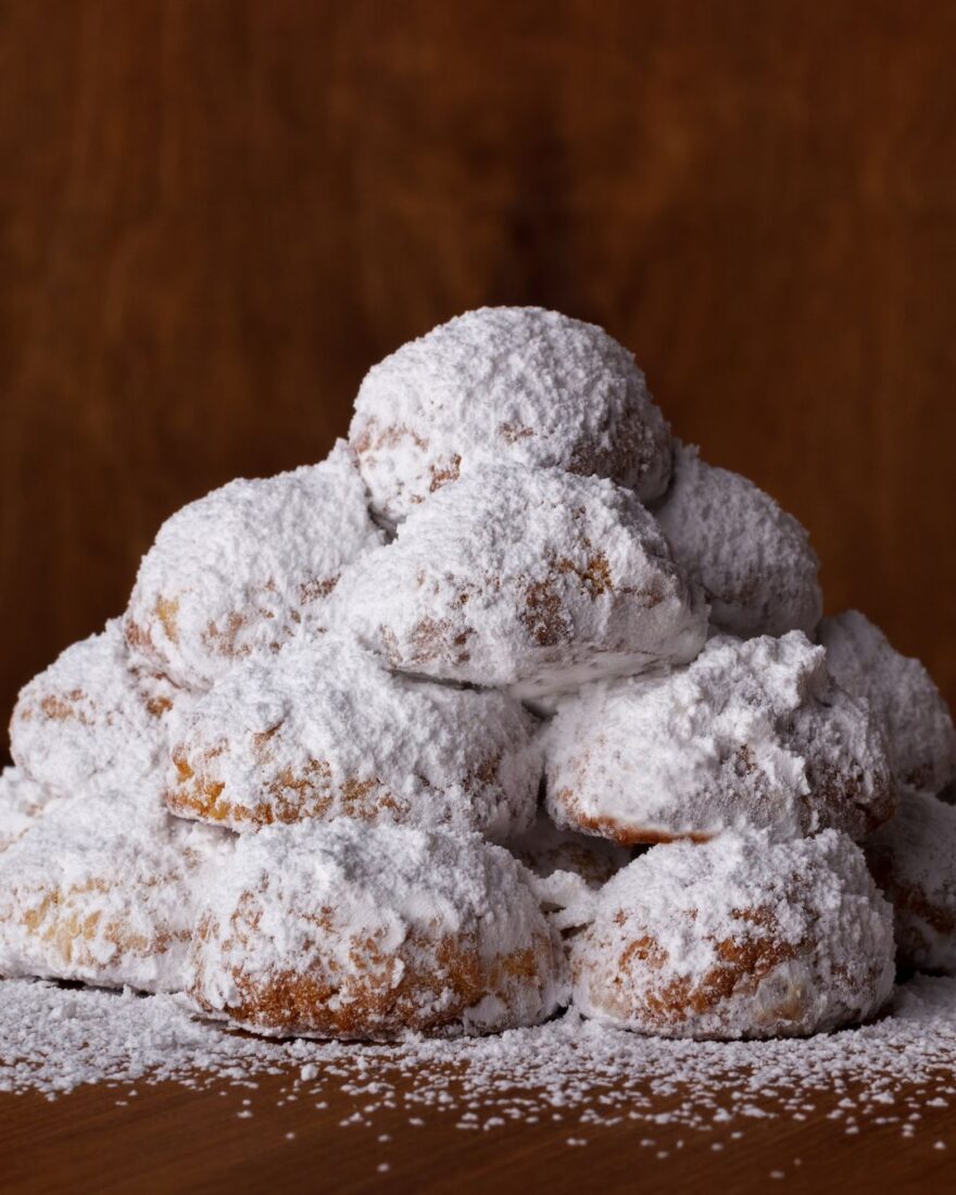 Kourabiedes Rezept – Griechische Butter-Mandeln-Kekse 3 Traditionelle griechische Kourabiedes mit viel Puderzucker vor dunklem Holz-Hintergrund