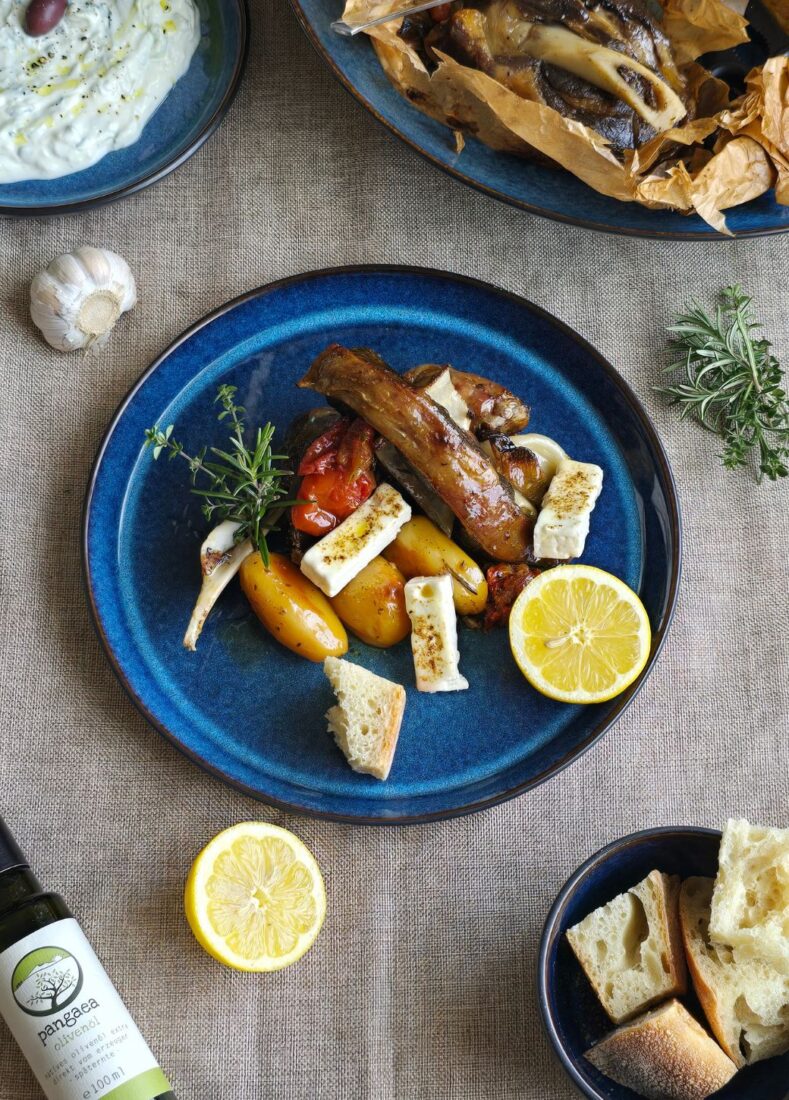 Zartes Ofenlamm mit Gemüse, Feta-Stücken, Brot und frischer Zitrone auf blauem Teller