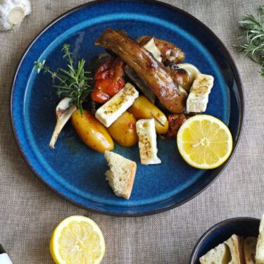 Kleftiko – Griechisches Lamm aus dem Ofen mit Kartoffeln, Kräutern & Pangaea Olivenöl 10 Zartes Ofenlamm mit Gemüse, Feta-Stücken, Brot und frischer Zitrone auf blauem Teller