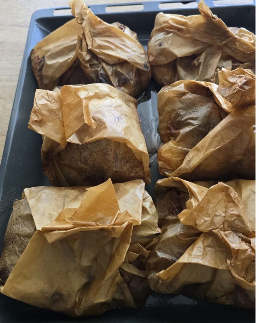 Sechs fertig gegarte Backpapierpäckchen mit Kleftiko auf einem Ofenblech