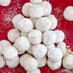 Kourabiedes Rezept – Griechische Butter-Mandeln-Kekse 4 Griechische Kourabiedes – zart mürbe Butterkekse mit Puderzucker auf rotem Untergrund