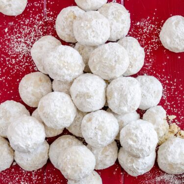 Kourabiedes Rezept – Griechische Butter-Mandeln-Kekse 4 Griechische Kourabiedes – zart mürbe Butterkekse mit Puderzucker auf rotem Untergrund