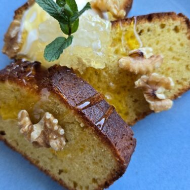 Olivenölkuchen Rezept – saftig, einfach & mit Joghurt 9 Saftiger Olivenölkuchen mit Honig, Walnüssen und Minze auf blauem Teller